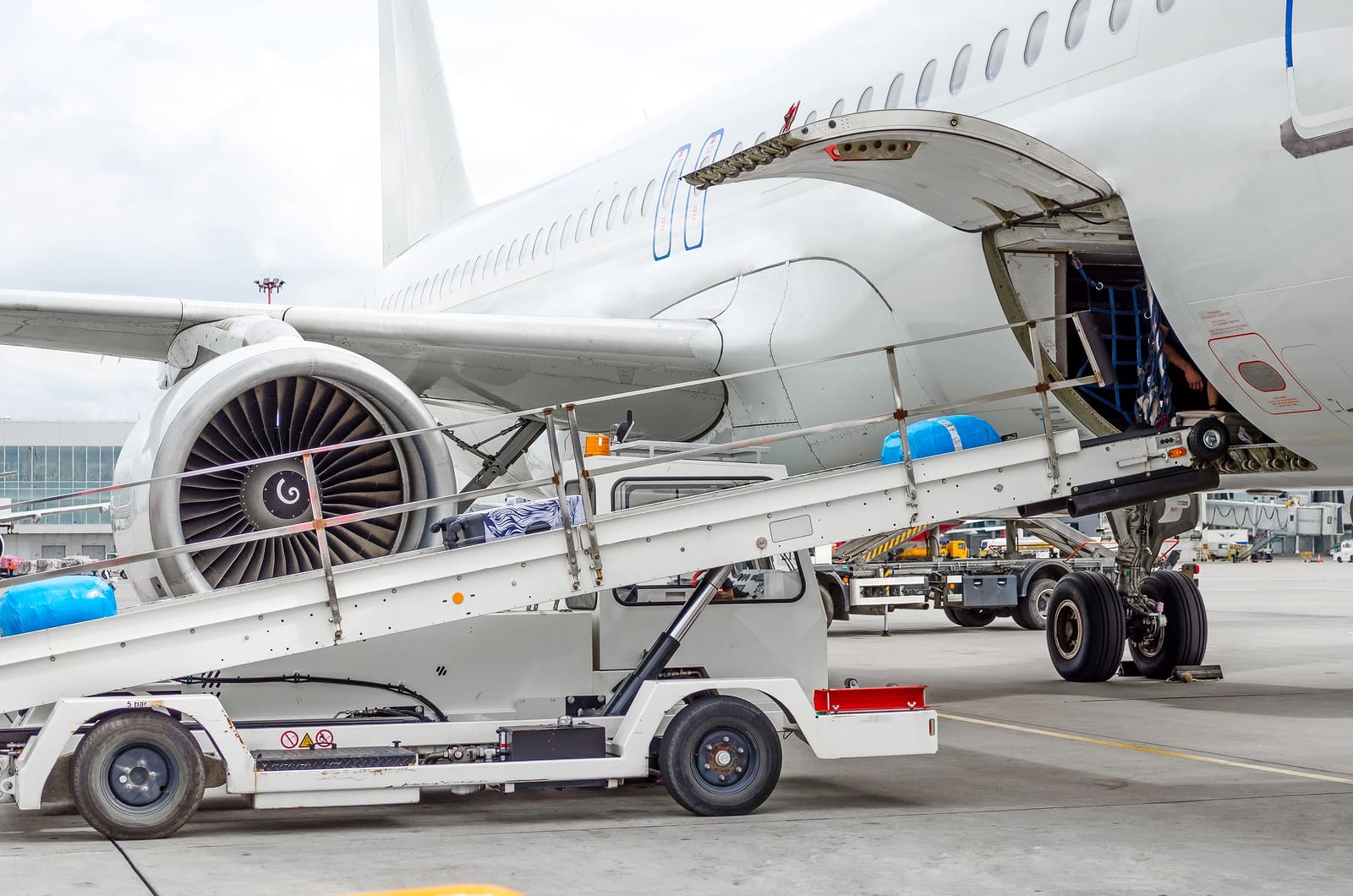 Belt loader at the open cargo hold of a passenger airliner on stand, with baggage being loaded during a turnaround